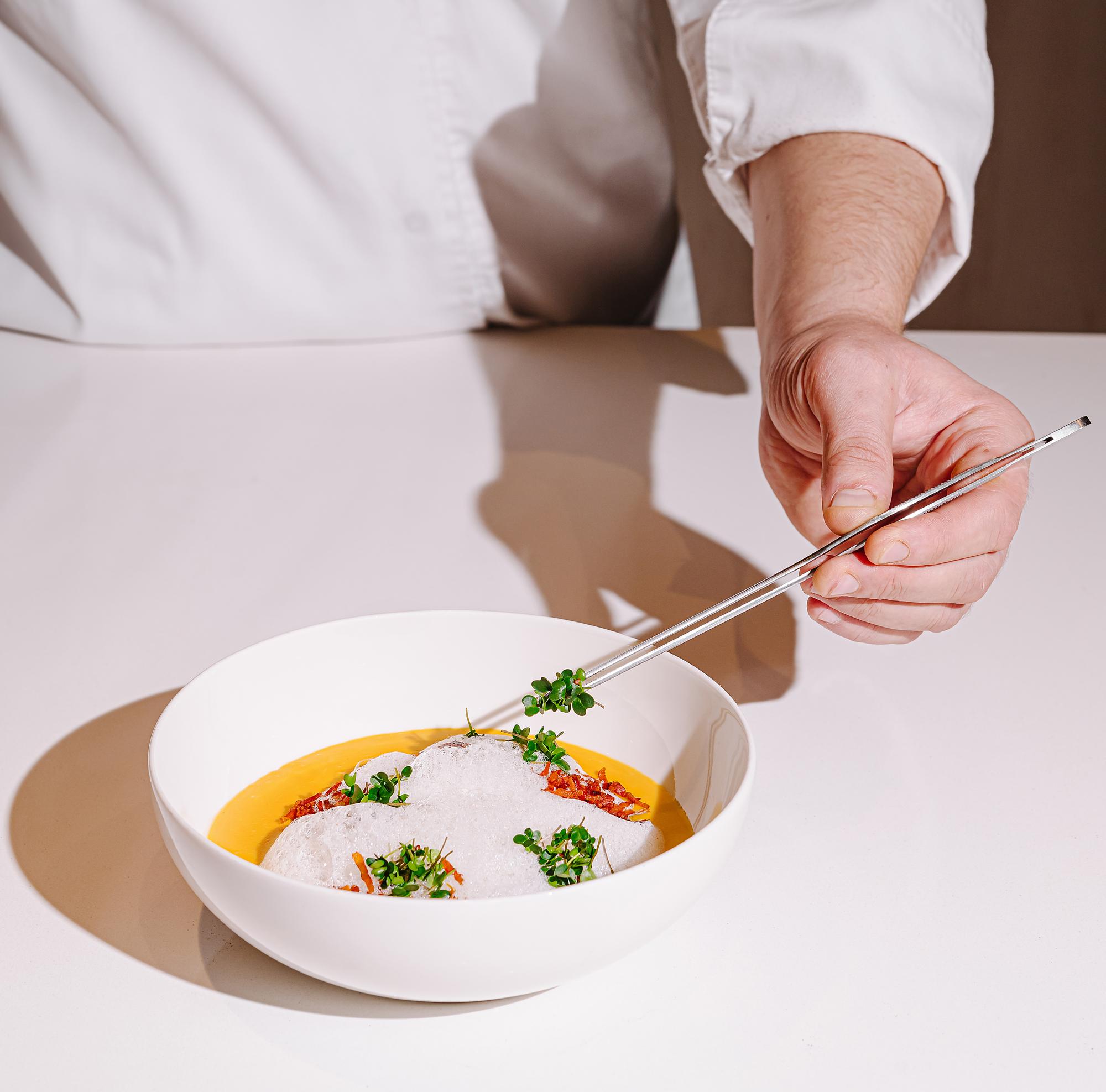 Chef plating a composed dish on a wooden table